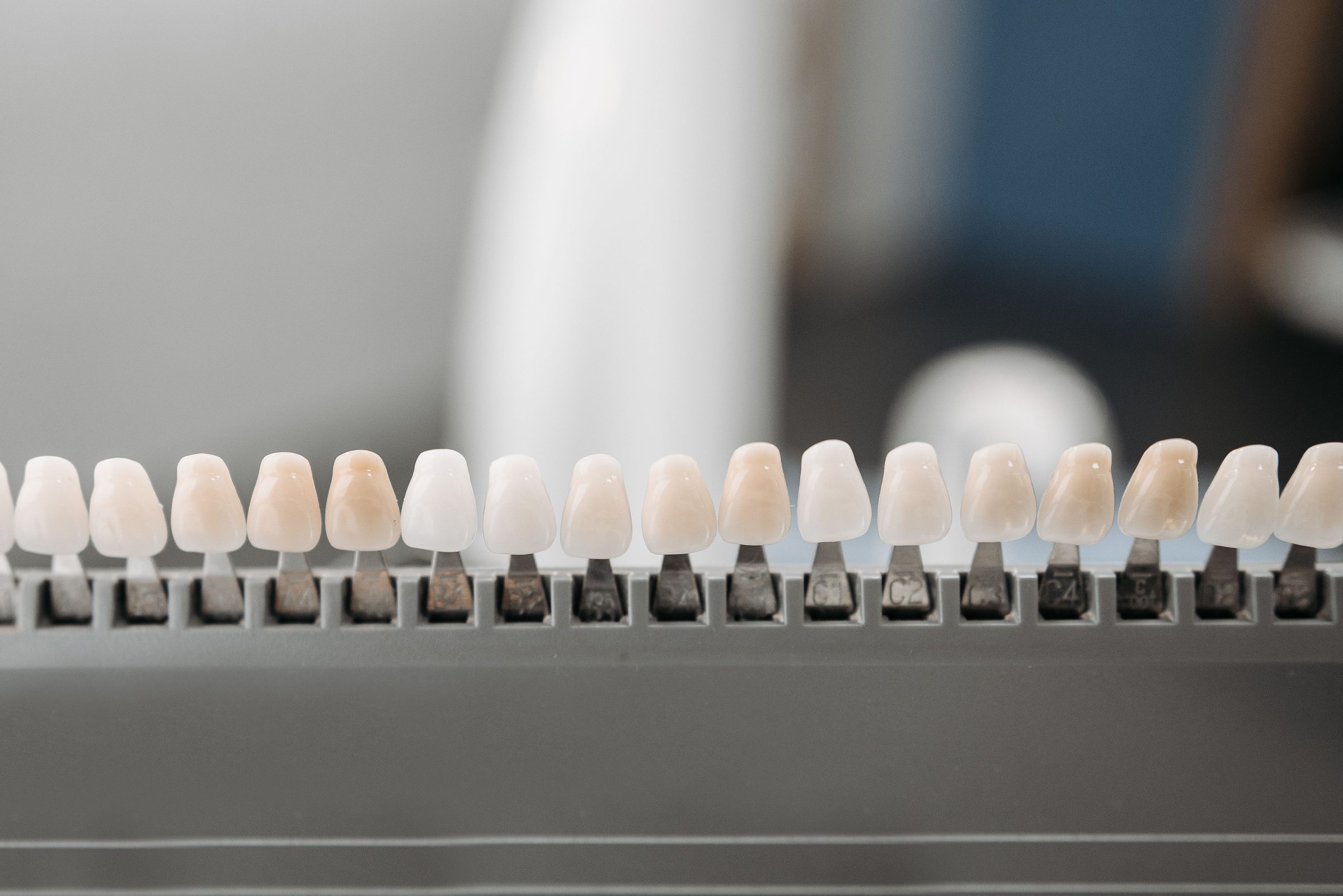 Mostruário de facetas dentárias alinhadas numa régua, em close.